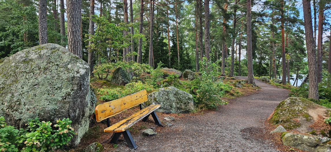 Grusggång genom skogen med en bänk och stora stenar, mellan Särstabadet och Pepparkaksudden