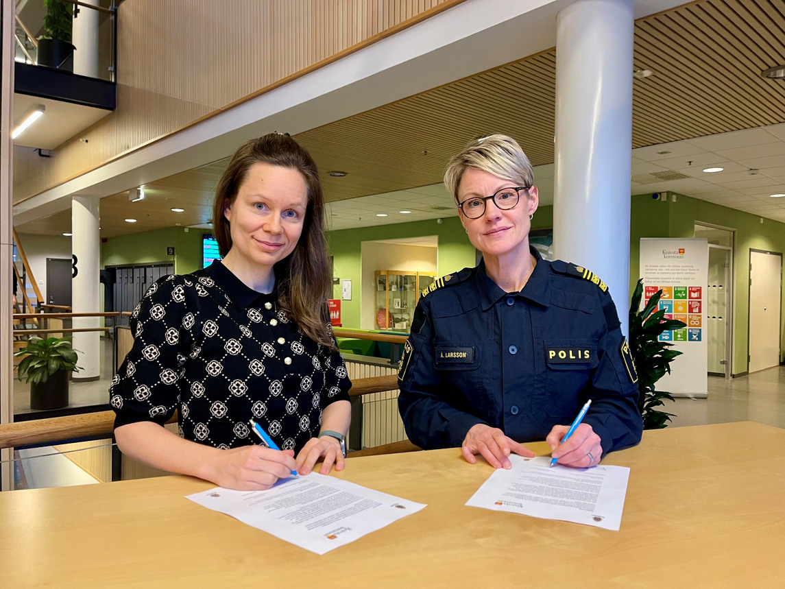 Två kvinnor står vid ett bord och signerar dokument. Den ena är klädd i polisuniform.