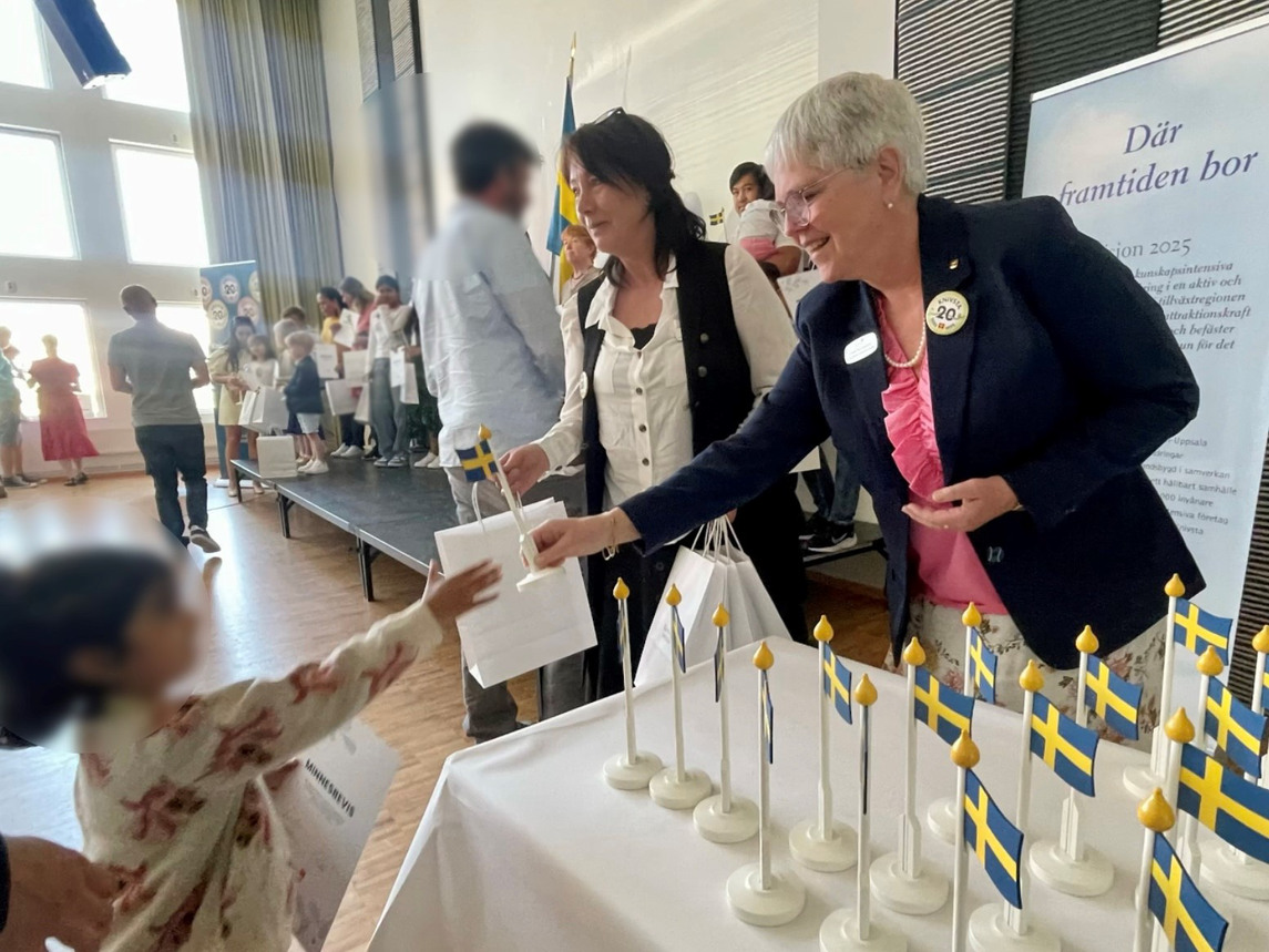 Maria Fornemo och Lisbeth Rye-Danjelsen delar ut en svensk flagga till en liten flicka
