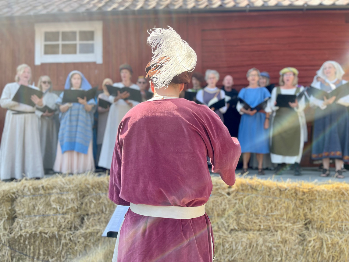 Dirigent framför Knivsta kammarkör, alla i medeltida kläder