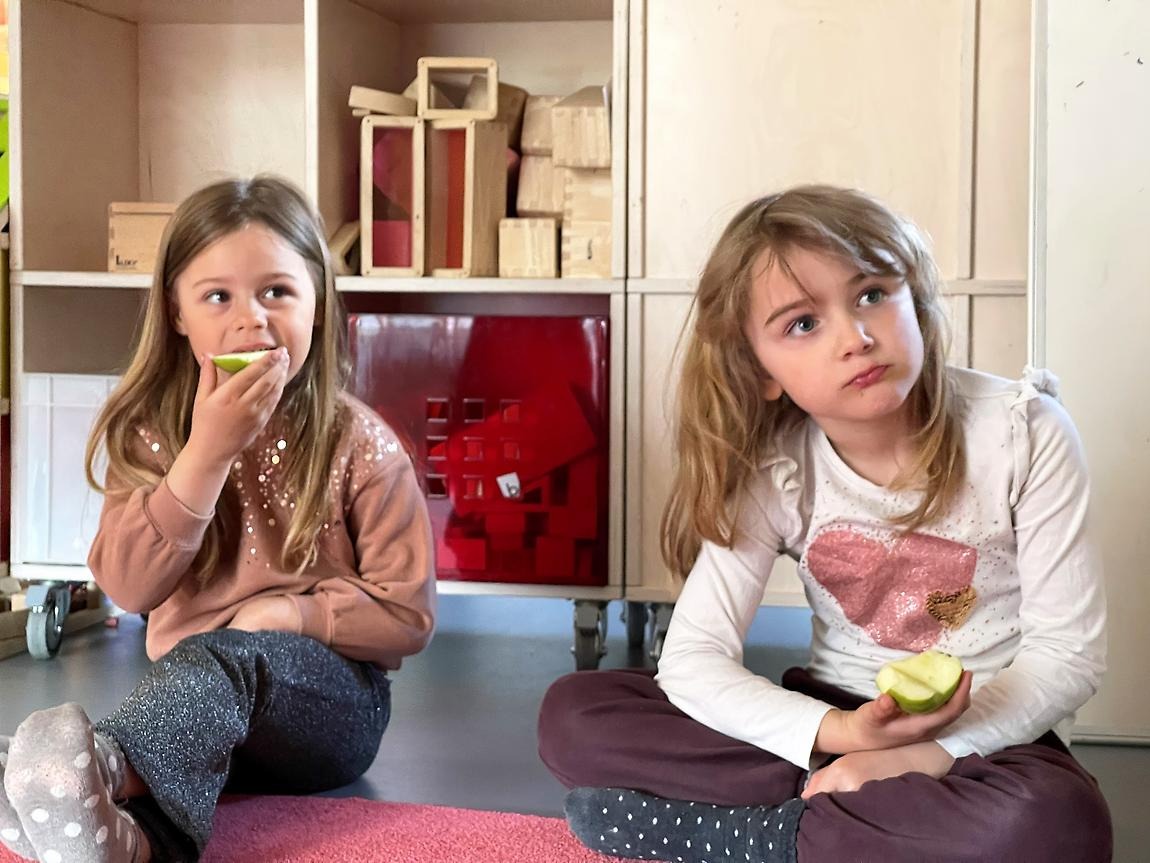 Två flickor sitter på golvet och äter äpple